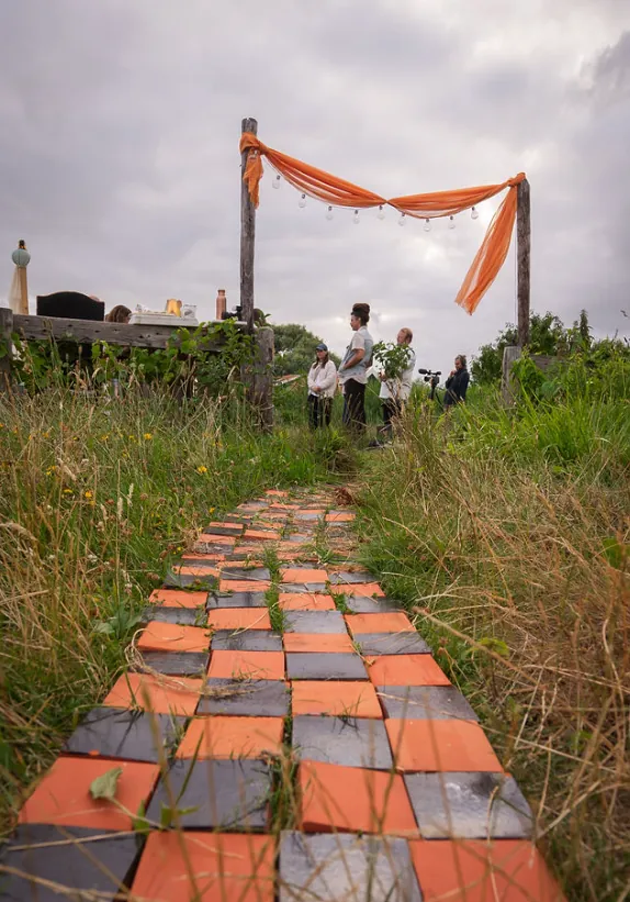 Checkered tile path through the meadow leading to an orange silk arch
