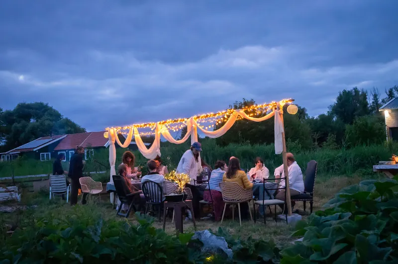 Guests dining at the long table under glowing string lights at blue hour